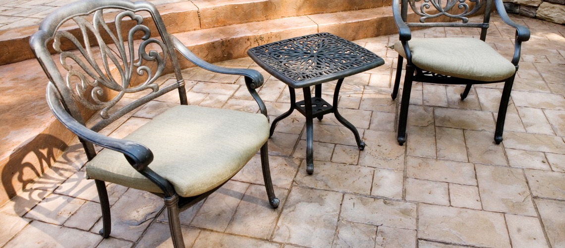 patio chairs with cushions flank a small matching side table on a stamped concrete patio